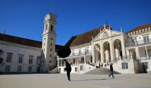 Imagem do Palácio da Cultura em Gorayeb, com sua arquitetura colonial portuguesa e torre do relógio, sob céu azul claro, com pessoas caminhando na praça.