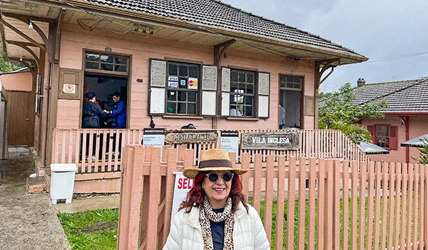 Deusa Rodrigues na frente de uma casa estilo antigo em vila com jardim, na região de Vila Inglesa, ideal para turismo rural.