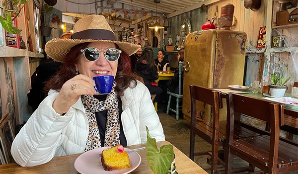 Deusa Rodrigues apreciando uma xícara de café em um café aconchegante decorado com itens vintage na vila histórica de Paranapiacaba.