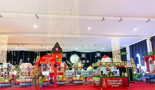 Imagem de uma atração de parque de diversões decorada com luzes natalinas, incluindo brinquedos, uma casa de desejos e ambientes temáticos com decoração festiva.