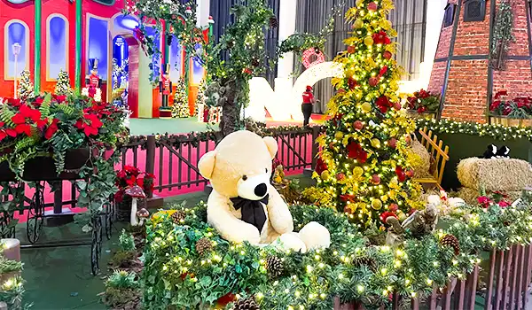 Decoração de Natal com urso de pelúcia, árvores decoradas, luzes natalinas e ambientes festivos em ambiente interno
