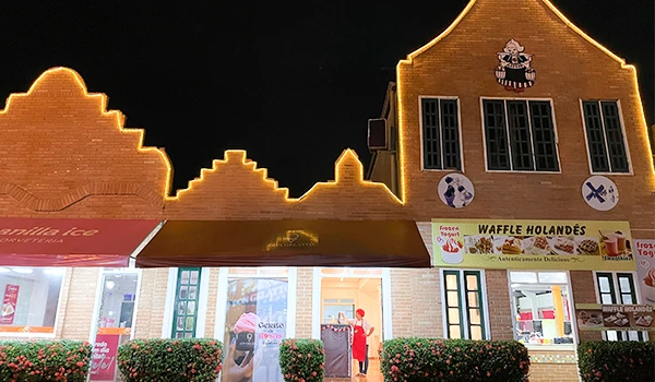 Fachada de uma loja de waffles chamada 'Waffle Holandês' em uma rua iluminada à noite, com detalhes decorativos na fachada e luzes de contorno.