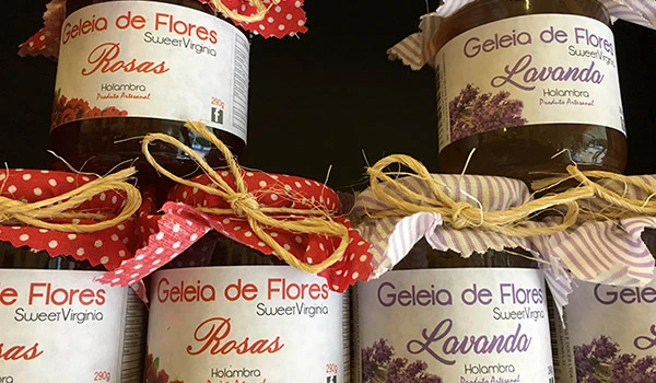 Imagem de potes de geleia de flores com sabores Rosa e Lavanda, decorados com fitas coloridas, perfeitos para presentear ou em ocasiões especiais.