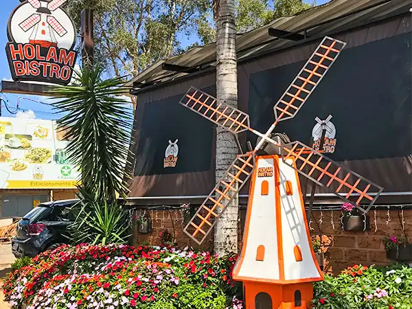 Imagem de uma fachada do Holam Bistro decorada com um moinho de vento de madeira e plantas de jardim, ideal para quem busca pratos saborosos e um ambiente acolhedor.