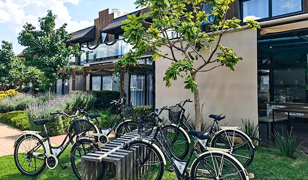Imagem de um condomínio moderno com bicicletas estacionadas em um espaço externo, cercado por árvores e plantas, em um ambiente ao ar livre bem cuidado.