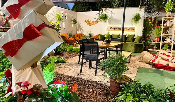 Imagem de um espaço externo decorado com móveis de jardim, plantas, sofá verde, mesa de centro, cadeiras, e elementos decorativos, ideal para ambientes ao ar livre.