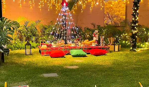 Decoração de Natal ao ar livre com uma árvore de Natal iluminada, almofadas coloridas e iluminação festiva, criando um ambiente aconchegante e natalino. Parada de Natal de Holambra.
