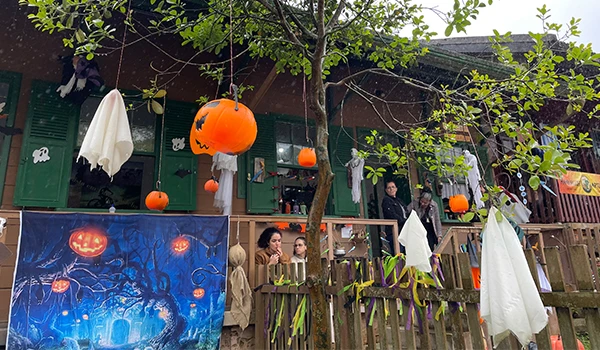 Decoração de Halloween ao ar livre com abóboras iluminadas, fantasmas de papel, e uma cena com crianças em um espaço festivo, ideal para festas de mês das bruxas.