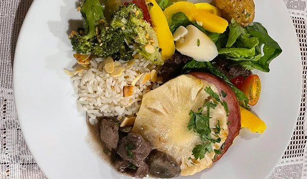 Prato de comida com arroz, brócolis, salada com pimentões e queijo, acompanhada de carne com molho.