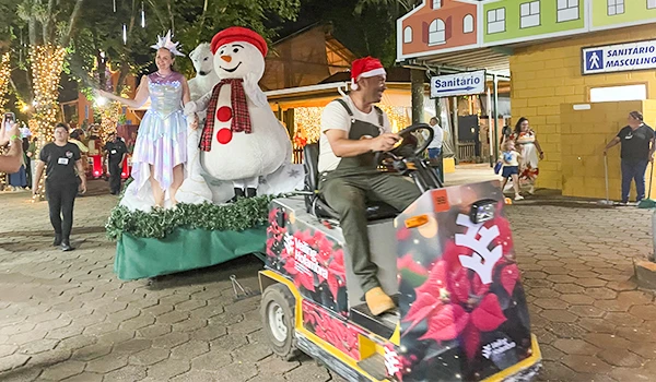 Desfile natalino na cidade com homens e mulheres em clima festivo, decorando ruas e celebrando o Natal com um trenó decorado e personagens festivos. Parada de Natal de Holambra.