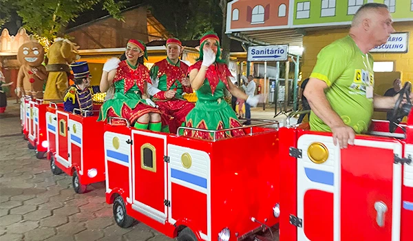 Família participando de um passeio natalino com carrinho de Natal decorado, coxinhas e figurinos de Natal, em ambiente externo durante a noite.