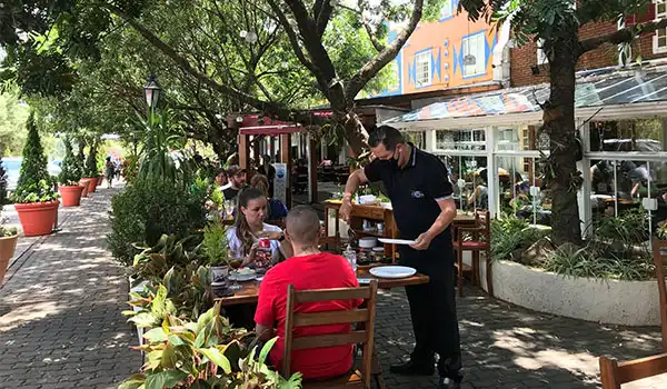 Família desfrutando de um almoço ao ar livre em um restaurante com ambiente paisagístico e atendimento de um garçom na fachada de um restaurante.