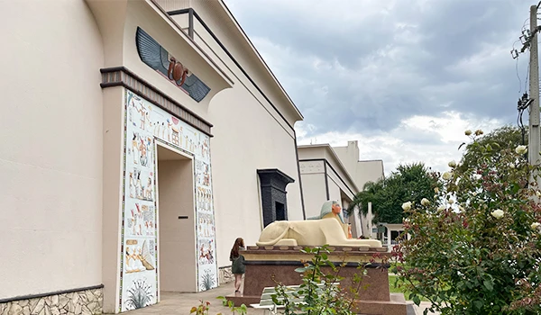 Imagem de uma residência moderna com detalhes arquitetônicos elegantes, jardim bem cuidado e uma escultura em frente à entrada, em um dia nublado. Museu Egípcio e Rosacruz em Curitiba.