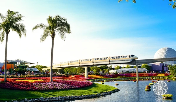 Imagem do Disney's EPCOT no mundo Disney, mostrando uma viagem de monorail sobre um lago cercado por jardins coloridos com flores e palmeiras, em um dia ensolarado.