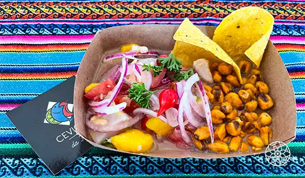 Salada de atum com cebola roxa, pimentões amarelos e tomates cereja, acompanhada de chips de milho, servida em uma bandeja de papel sobre uma toalha colorida, ideal para refeições leves e saudáveis.