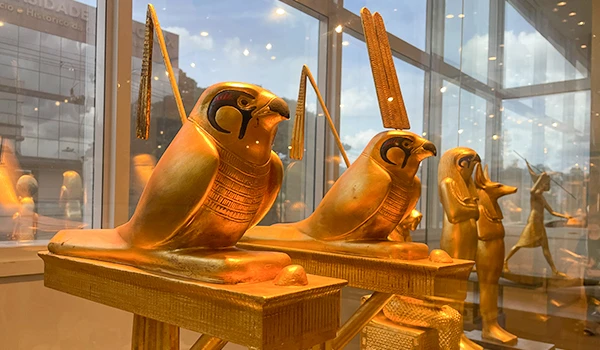 Estátuas douradas de pássaros gípcios em uma exposição, evidenciando detalhes do artesanato com iluminação suave ao fundo.