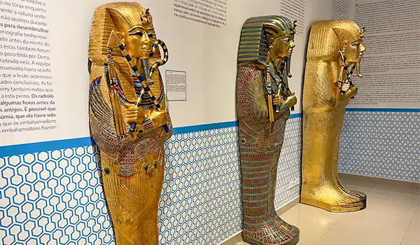 Esculturas de ouro de faraós egípcios em um museu, destacando detalhes elaborados, cores vibrantes e referências à cultura antiga do Egito.