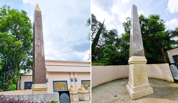Obelisco decorativo localizado em um ambiente ao ar livre, cercado por árvores verdes e com paredes ao fundo, em uma área de turismo ou lazer no Brasil.