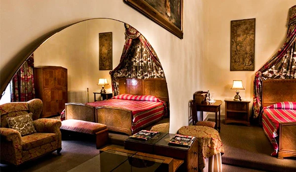 Imagem de um confortável quarto de hotel com duas camas, poltronas e decoração vintage, perfeito para uma estadia relaxante.