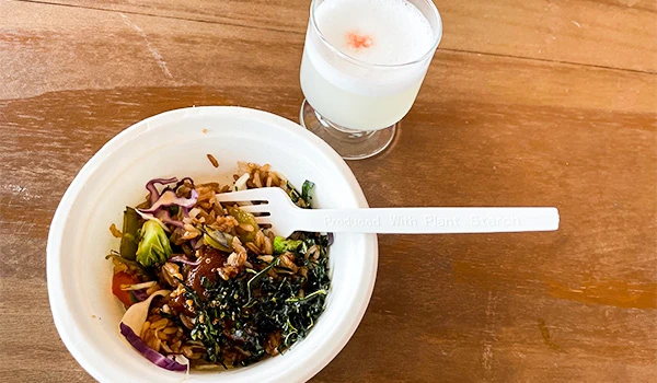 Prato de comida asiática com noodles, legumes e molho, acompanhado de uma bebida branca em um copo de vidro. Perú Mucho Gusto pratos típicos.