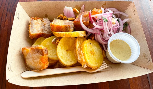 Imagem de comida com pão de alho, costelinha de porco e salada de cebola, acompanhada de molho. Perú Mucho Gusto pratos típicos.