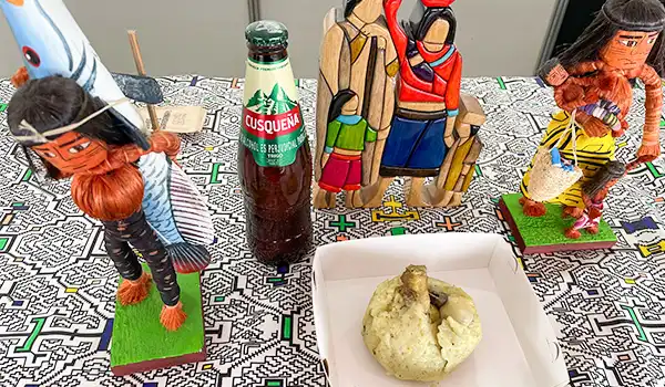 Imagem de figuras de piratas de madeira, uma bebida de refrigerante e uma maçã partida, apresentando elementos característicos de uma comemoração. Perú Mucho Gusto pratos típicos.