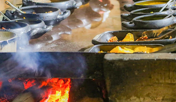 Diversas panelas de ferro com alimentos cozinhando sobre uma fogueira de lenha, evidenciando uma típica culinária ao ar livre, com foco na preparação de pratos tradicionais.