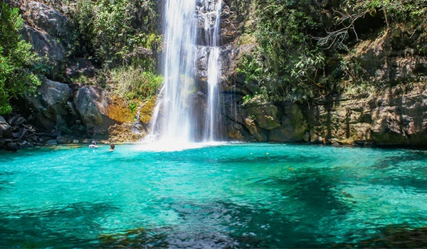 Cachoeira em uma paisagem de natureza com água cristalina de cor azul turquesa e vegetação ao redor, criando um cenário tranquilo e exuberante. Turismo na Chapada dos Veadeiros.