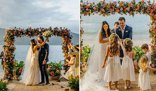 Casal de noivos celebrando casamento ao ar livre na praia com decoração de flores. Momento romântico e feliz na cerimônia de casamento ao pôr do sol.