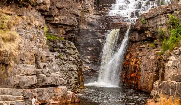 Cachoeira em uma formação rochosa, com água caindo suavemente em uma piscina natural, cercada por rochas e vegetação, ideal para turismo de natureza no Brasil. Turismo na Chapada dos Veadeiros.