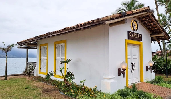Capela com arquitetura simples e charmosa, rodeada por árvores e vista para um lago, ideal para cerimônias ao ar livre em ambiente natural. Ilhabela turismo e casamentos.