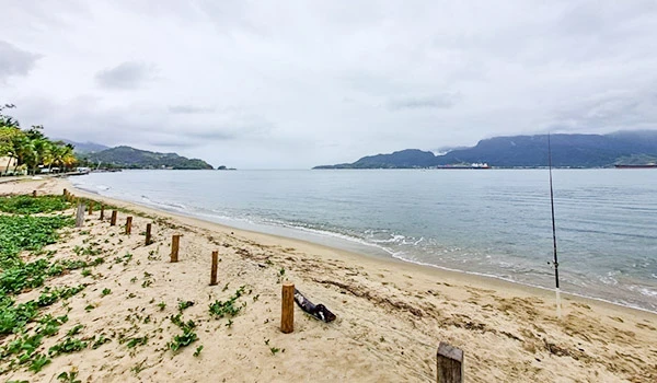 Praia tranquila com areia clara, cercada por verdejantes áreas de vegetação e vista para o mar, ideal para lazer e pesca, com céu parcialmente nublado. Ilhabela turismo e casamentos