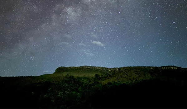 Céu estrelado sobre uma paisagem escura com estrelas brilhando intensamente, ideal para observação astronômica e atividades ao ar livre noturnas. Turismo na Chapada dos Veadeiros.