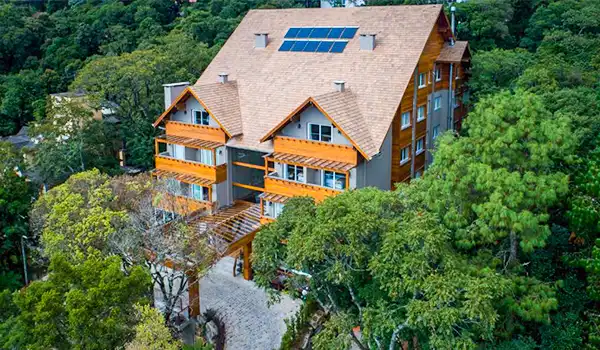 Linda casa de arquitetura moderna rodeada por árvores verdes, com painéis solares no telhado e varanda na frente, localizada em uma área de natureza exuberante no Brasil.