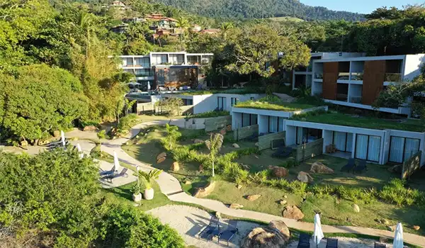 Imagem de um hotel sustentável com casas modernas e áreas verdes bem cuidadas, localizado em um ambiente arborizado e tranquilo, ideal para quem busca luxo e conforto em meio à natureza.