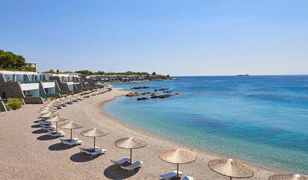 Praia com cadeiras de descanso sob guarda-sóis, águas calmas e ambiente tranquilo, perfeito para relaxar. Onde ficar na Grécia.