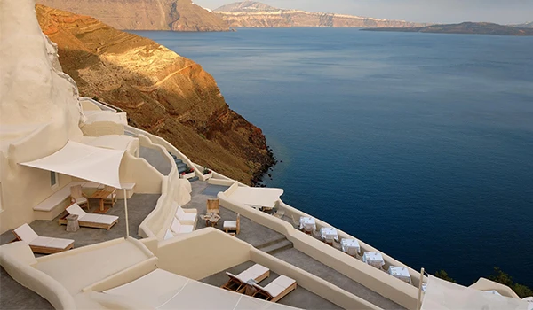 Vista deslumbrante de um resort à beira do mar com cadeiras de praia brancas e uma parede de falésia ao fundo, localizado em uma ilha de clima ensolarado.