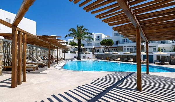 Piscina em um resort com espreguiçadeiras, guarda-sóis de palha, palmeiras e edifícios residenciais modernos ao fundo, ambiente de lazer ao ar livre.