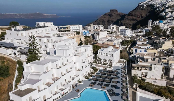 Vista aérea de Santorini com casas brancas, piscina e horizonte do mar, mostrando a beleza de um destino turístico conhecido na Grécia.