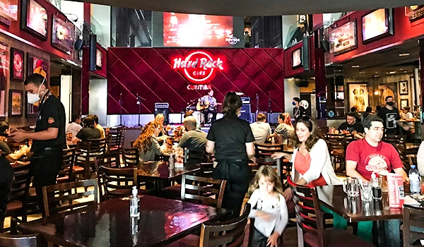Ambiente do Hard Rock Cafe Curitiba com clientes aproveitando comida e música ao vivo em um espaço moderno e animado, decorado com elementos musicais.