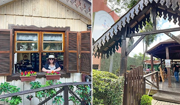 Imagem de uma mulher sorridente usando chapéu e óculos de sol, posando na janela de uma casa de madeira com jardim de flores na frente, ambiente ao ar livre