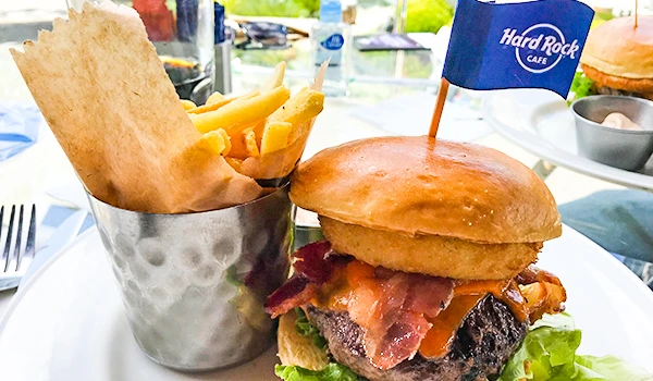 Hambúrguer gourmet com bacon, queijo, alface, tomate, e um pão macio, acompanhado de porções de batatas fritas crocantes em um restaurante.