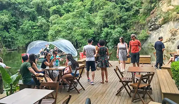 Turistas desfrutando de um passeio ao ar livre em uma área com deck de madeira, cercada por vegetação exuberante e vista para o rio, em um ambiente de natureza e lazer.
