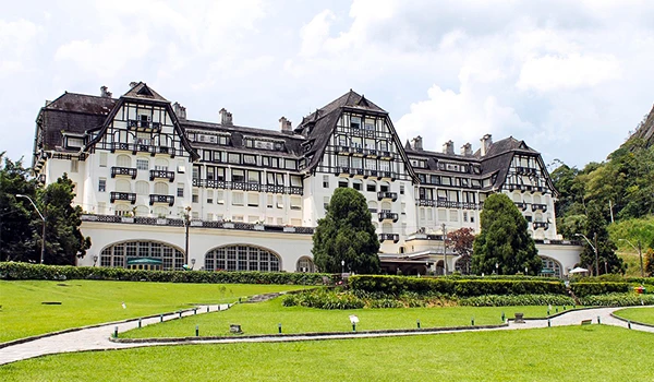 Hotel de luxo em um cenário de natureza com jardins bem cuidados e árvores ao redor, imóvel de grande porte com arquitetura elegante e detalhes clássicos.