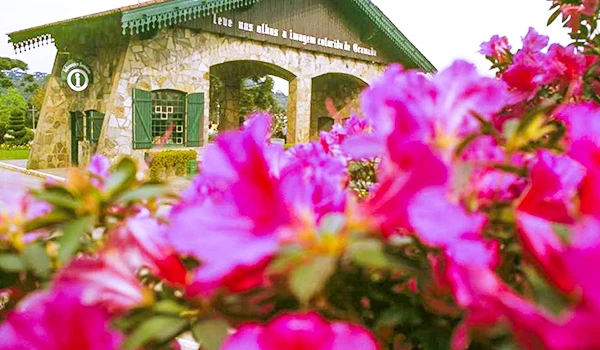 Imagem da Casa de Cultura do Guarujá com flores pink em primeiro plano e fachada de pedra ao fundo