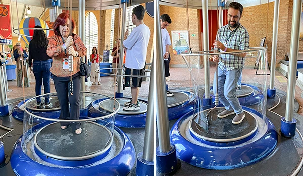 Pessoas se divertindo fazendo bolhas de sabão gigante com estrutura de supporte de vidro e cores vibrantes, em um ambiente de parque de diversões. Atrações do Museu Catavento.