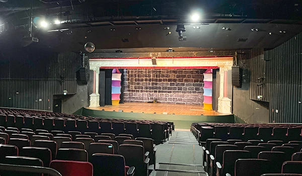 Auditório com palco preparado para apresentações, teatro ou eventos culturais, com cadeiras em fila e iluminação adequada.
