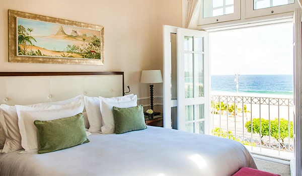 Quarto de hotel com vista para o mar, decoração aconchegante com cama com travesseiros verdes, abrir janela para vista oceânica, ambiente relaxante. Um dos hotéis de luxo do Rio de Janeiro.
