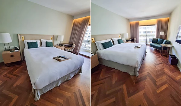 Imagem de um quarto de hotel moderno com cama de casal, cabeceira estofada, iluminação suave, cortinas ao lado de uma janela grande e piso de madeira parquet. Ideal para viagem de lazer ou negócios.