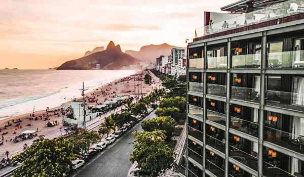 Uma vista deslumbrante da orla de Ipanema no Rio de Janeiro ao entardecer, com o Morro Dois Irmãos ao fundo e edifícios modernos ao lado da praia movimentada. Perfeita para quem busca imagens da cidade maravilhosa.